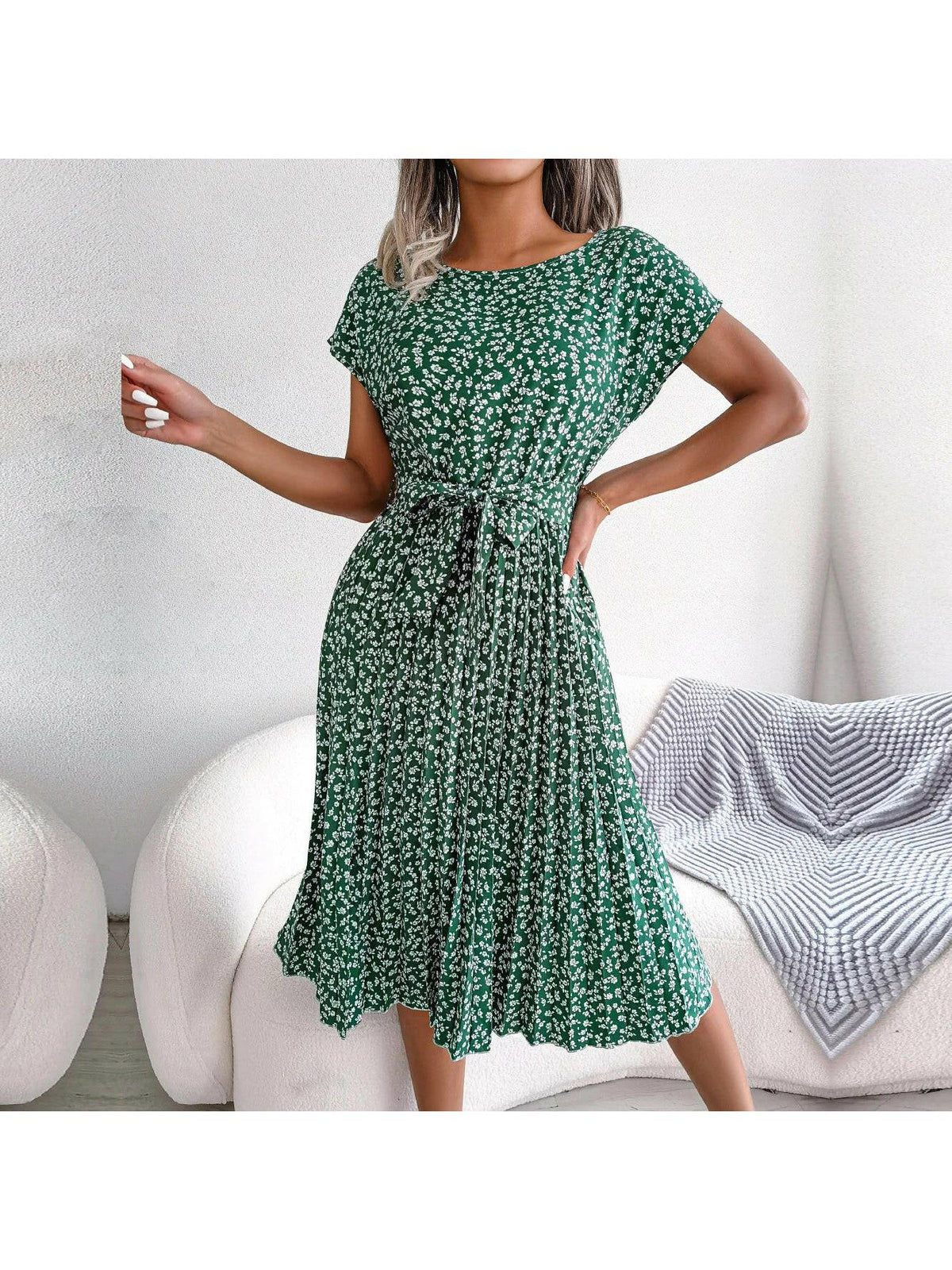 Woman wearing a green floral midi dress with pleated skirt and waist tie, front view