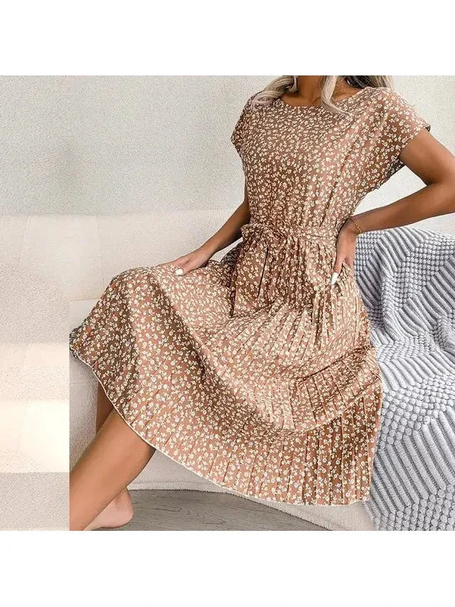 Woman seated in a light-brown floral midi dress with pleated skirt and waist tie