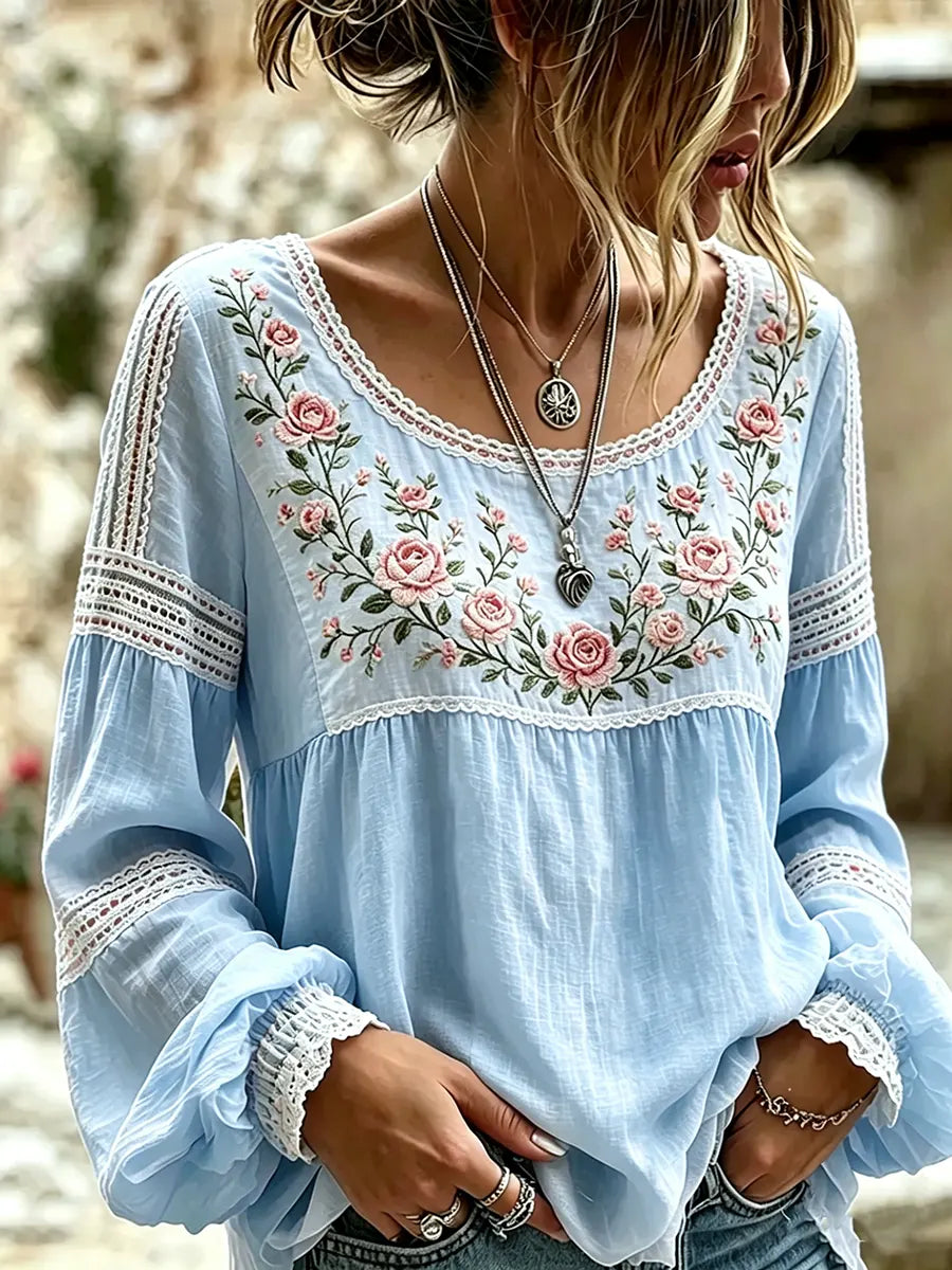 Blue blouse with rose embroidery, a rounded neckline and lace-trimmed sleeves