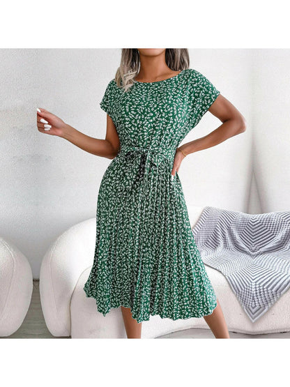 Woman wearing a green floral midi dress with pleated skirt and waist tie, front view