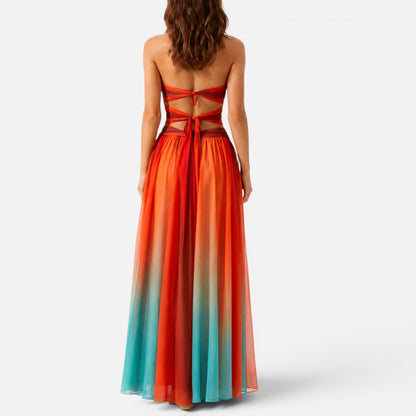 Woman wearing a strapless red-and-orange ombré maxi dress with waist cut-outs, rear view showing tied open back