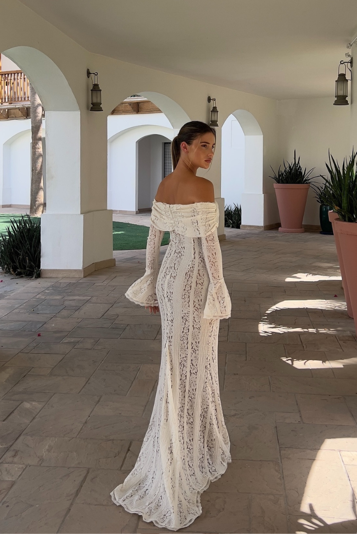 Woman wearing a white off-shoulder lace maxi dress with fluted sleeves, rear view outdoors