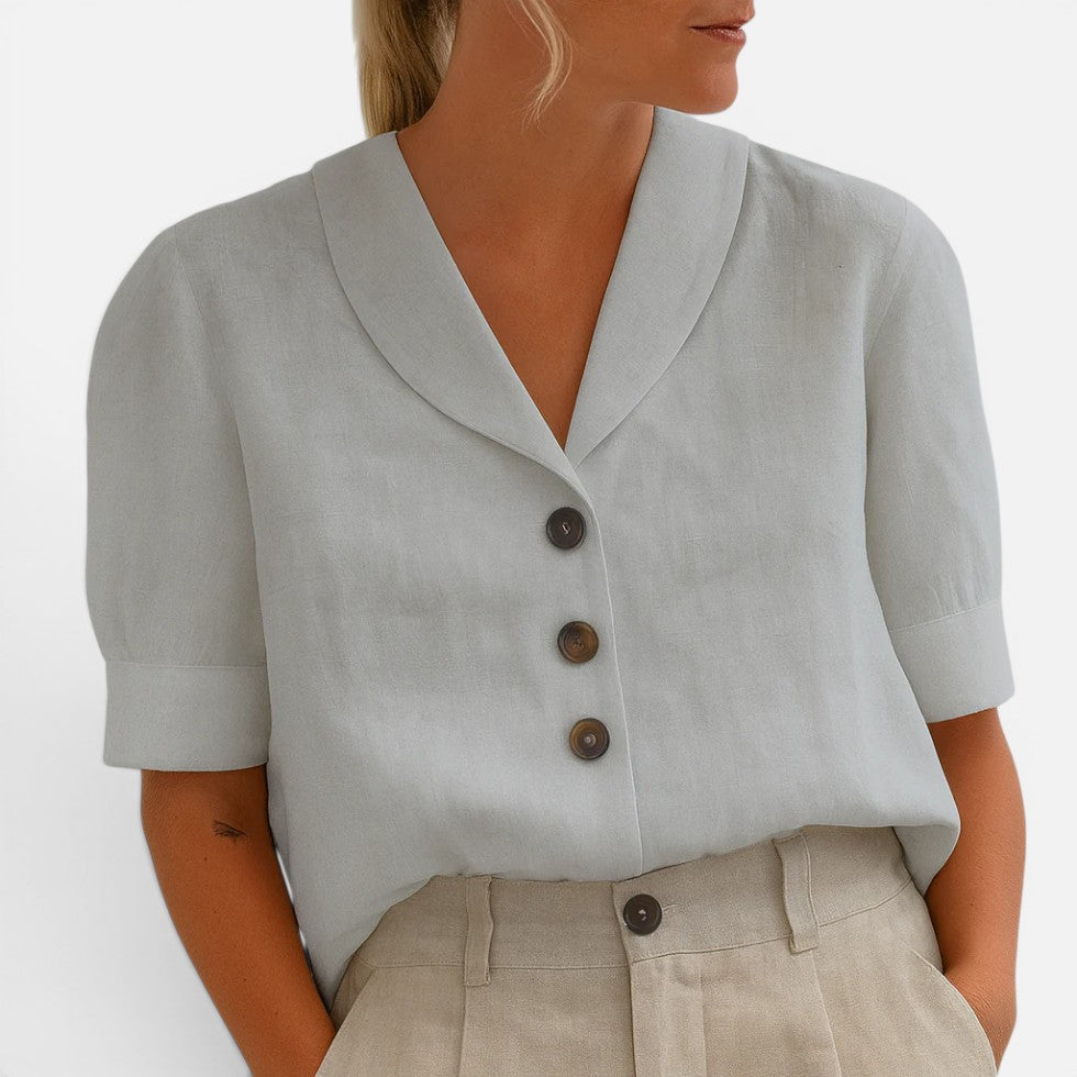 Woman wearing a light-grey short-sleeve blouse with a V-shaped collar and three-button front