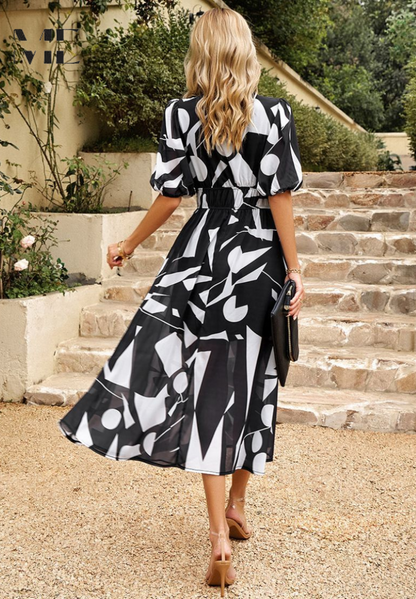 Woman wearing a black-and-white geometric-print V-neck midi dress, rear view