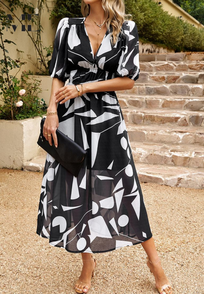 Woman wearing a black-and-white geometric-print V-neck midi dress holding a clutch