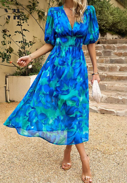 Woman wearing a blue-and-teal abstract floral V-neck midi dress with flowing skirt